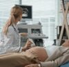 Gynecologist performing abdominal ultrasound scan on female patient to assess causes of irregular menstrual cycles.